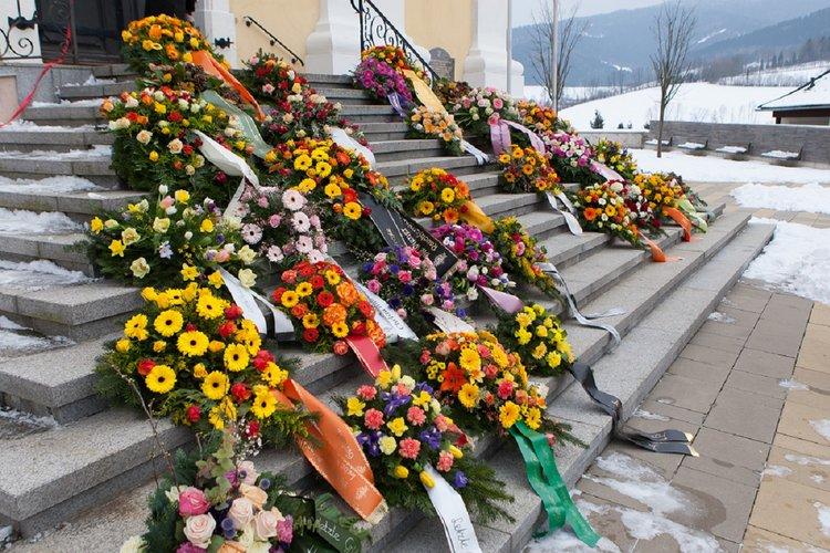 Paljon kukkalaitteita kirkon portailla talvisessa maisemassa.